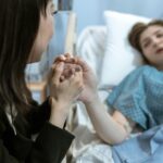 Woman holding patient's hand in hospital, providing comfort and care.